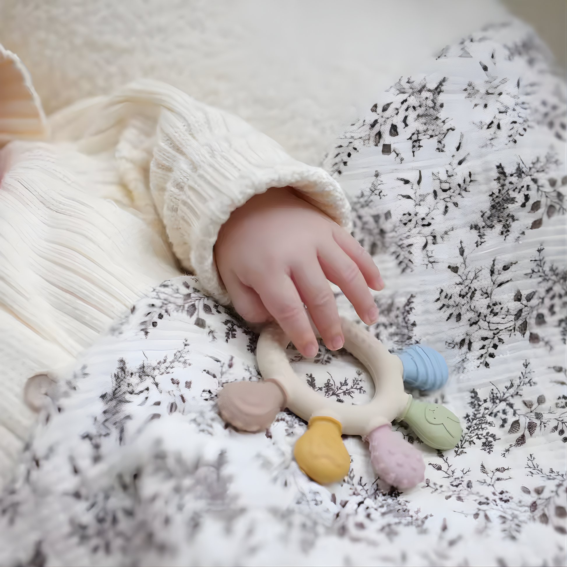 Main d’un bébé tenant un anneau de dentition posé sur un tissu à motifs