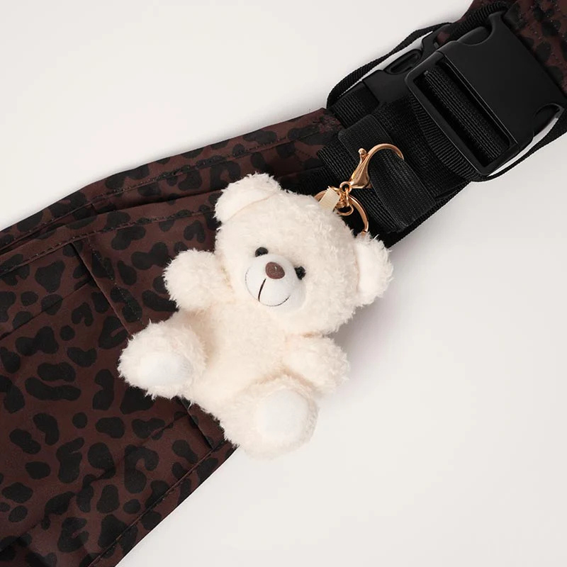 Doudou ours blanc avec mousqueton accroché sur un porte-bébé à motif léopard, accessoire de portage doux et rassurant
