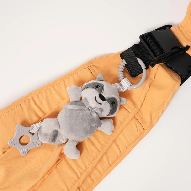 Doudou raton laveur gris fixé sur un porte-bébé orange avec attache sécurisée et anneau de dentition pour bébé
