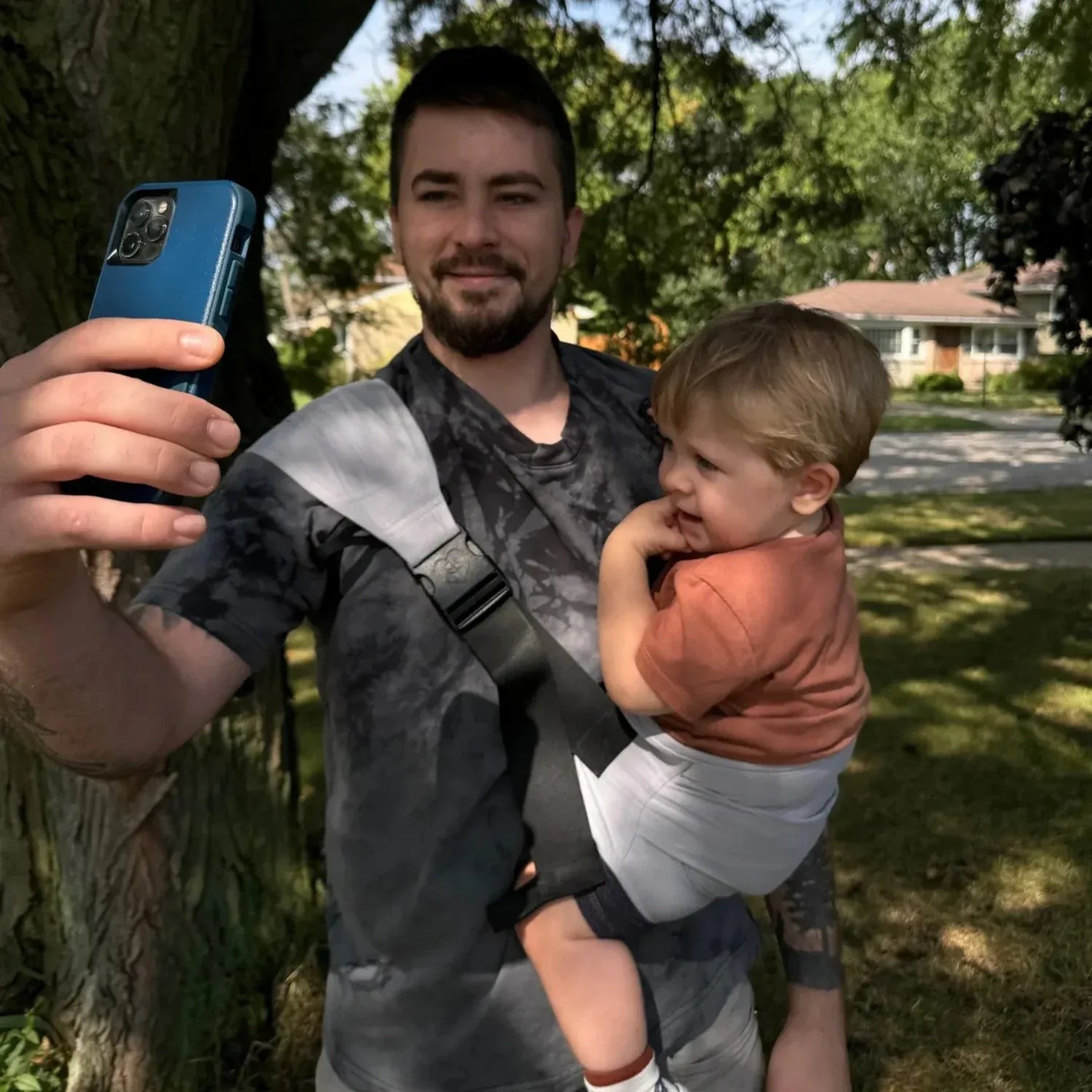 Papa portant son bébé de quelques mois dans le porte-bébé HelloBiboo lors d’une promenade en extérieur, bébé calmé et bien installé contre lui.