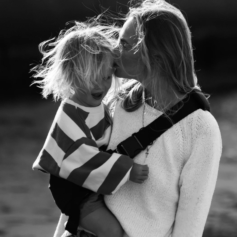 Maman portant son fils de 3 ans dans un porte-bébé physiologique HelloBiboo, moment de tendresse en extérieur