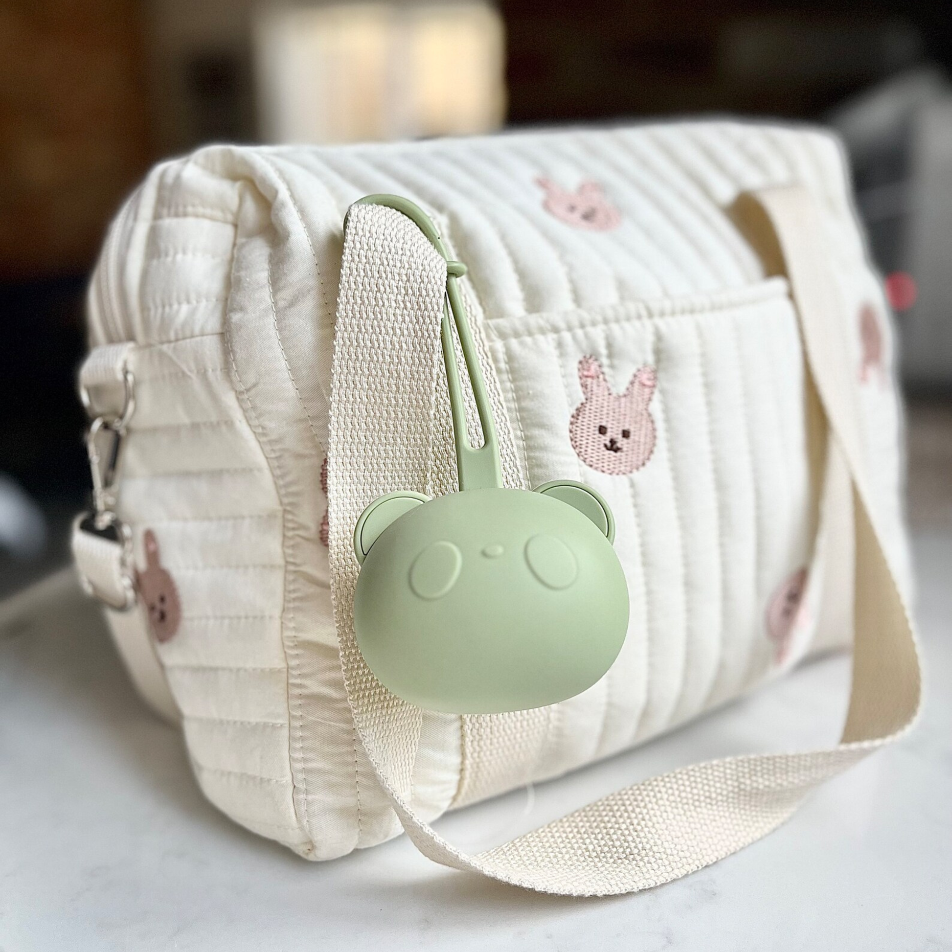 Porte-tétine en silicone vert accroché à un sac à langer beige décoré de motifs lapins