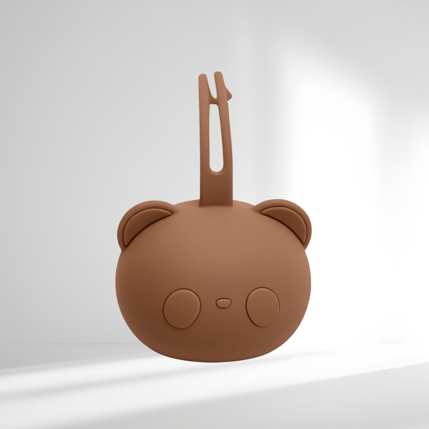Porte-tétine en silicone marron en forme d’ourson, présenté sur un fond lumineux